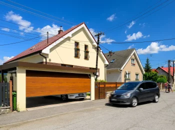 Eleganter Carport mit braunem Tor und gelbem Putz, der das Fahrzeug schützt.