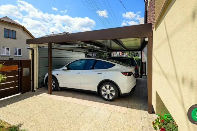 Autos geschützt unter einem Carport mit geschlossenem breitem Garagentor.