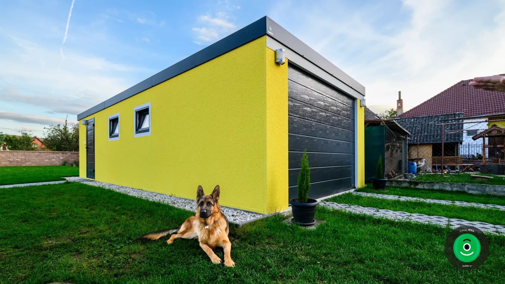 Ein Hund sitzt vor einer Garage mit gelbem Putz