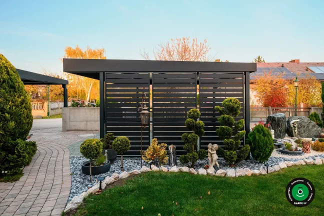 Seitenwand des Unterstands bei Ziergehölzen und Kies