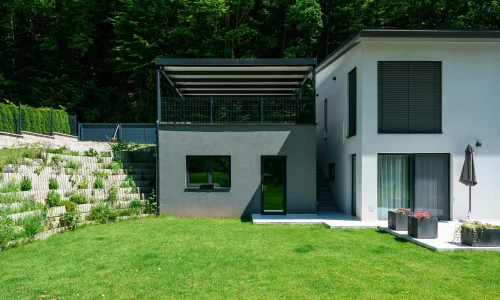 Anthrazitfarbene Pergola mit Pultdach auf erhöhtem Untergrund montiert.