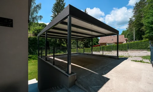 Dunkelgraues Carport mit Flachdach und Attika am Einfamilienhaus.