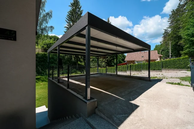 Dunkelgraues Carport mit Flachdach und Attika am Einfamilienhaus.