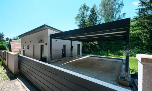 Offenes Carport mit anthrazitfarbenem Flachdach am weißen Einfamilienhaus.