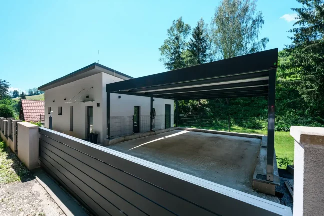 Offenes Carport mit anthrazitfarbenem Flachdach am weißen Einfamilienhaus.