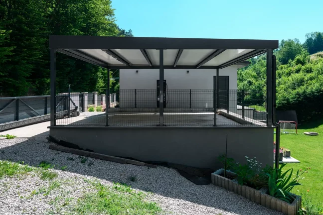 Carport mit anthrazitfarbenem Flachdach auf erhöhter Terrasse am Garten.