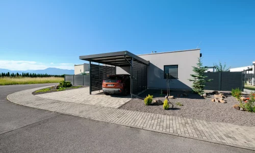 Anthrazitfarbenes Vordach mit Metallfüllung am Einfamilienhaus mit gepflasterter Einfahrt.