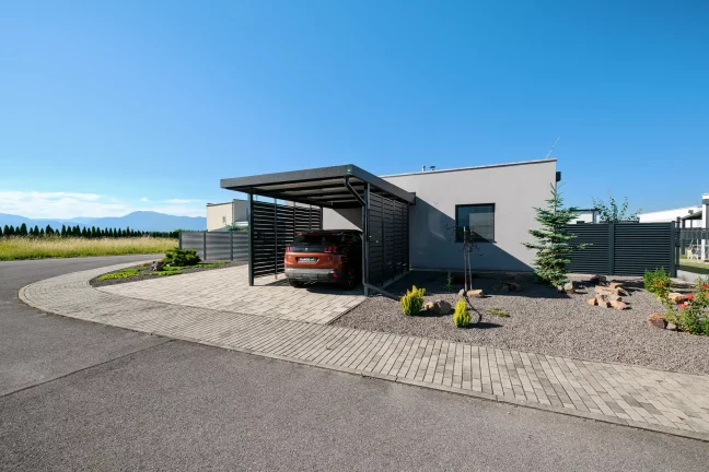 Anthrazitfarbenes Vordach mit Metallfüllung am Einfamilienhaus mit gepflasterter Einfahrt.