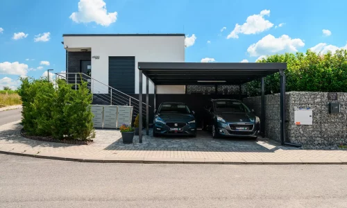 Anthrazitfarbener Flachdach-Carport mit Seitenwand an modernem Wohnhaus.
