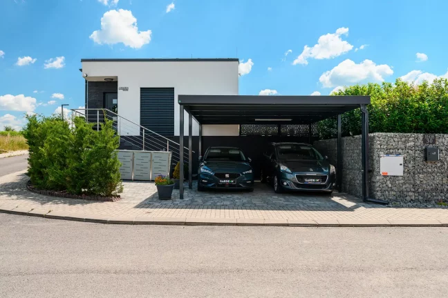 Anthrazitfarbener Flachdach-Carport mit Seitenwand an modernem Wohnhaus.
