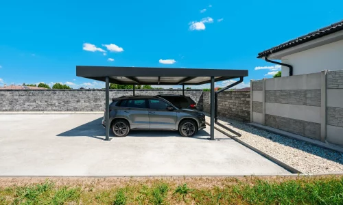 Zwei SUV parken unter anthrazitfarbenem Carport mit Flachdach am Haus.