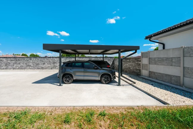 Zwei SUV parken unter anthrazitfarbenem Carport mit Flachdach am Haus.