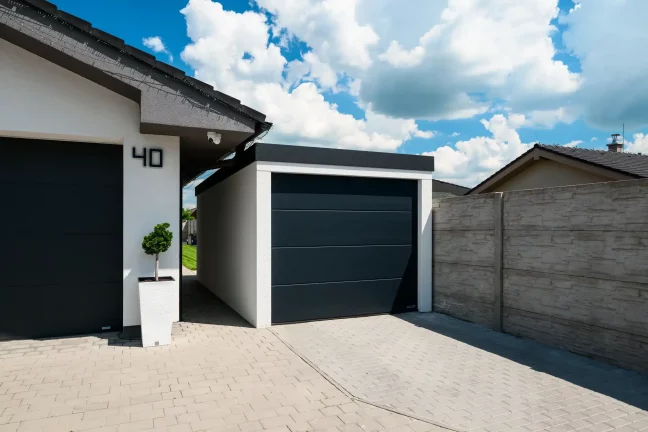 Detail einer weißen Garage mit anthrazitfarbenem Pultdach, dunkles Sektionaltor