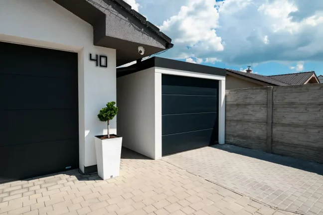 Weiße Garage mit anthrazitfarbenem Pultdach, dunklem Sektionaltor und dekorativer Pflanze am Eingang