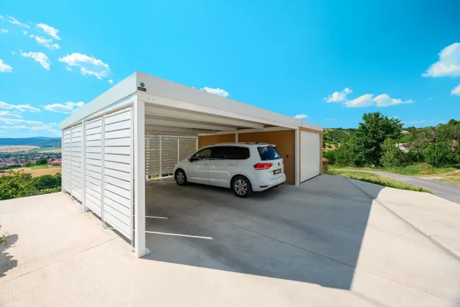 Carport mit weißer Metallverkleidung und angeschlossener Garage mit Ziegelputz, geparktes Auto.