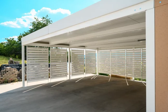 Horizontale weiße Metallverkleidung eines großen Carports bei einem Einfamilienhaus.