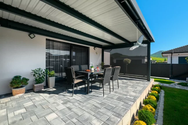 Blick aus dem Inneren der Pergola auf Gartenmöbel und Terrassenplatten, anthrazitfarbene Konstruktion mit Rollos