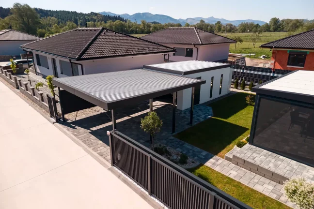 Anthrazitfarbene Garage mit Carport für ein Auto, Drohnenaufnahme der gepflasterten Einfahrt