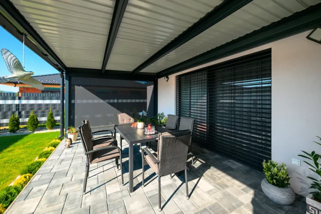 Innenansicht einer Pergola mit Lamellendach, Gartenstühle und Blick auf den grünen Garten