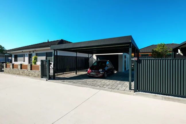 Anthrazitfarbene Garage mit Carport und Pergola, Frontansicht mit offenem Tor und gepflasterter Fläche