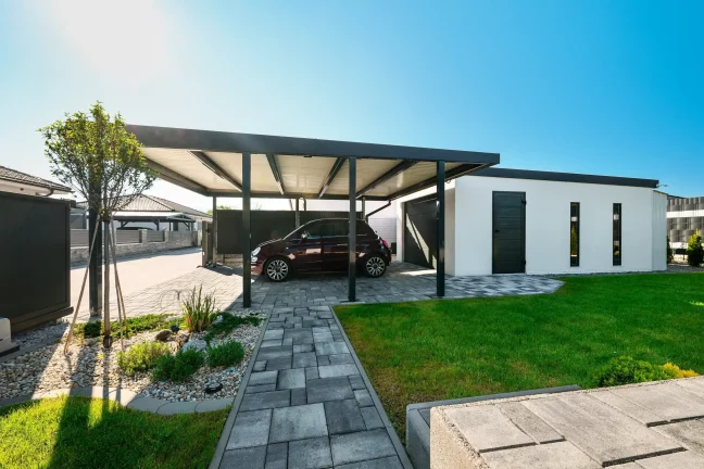 Rotes Auto unter einem anthrazitfarbenen Carport mit Pultdach neben einem dunklen Zaun geparkt