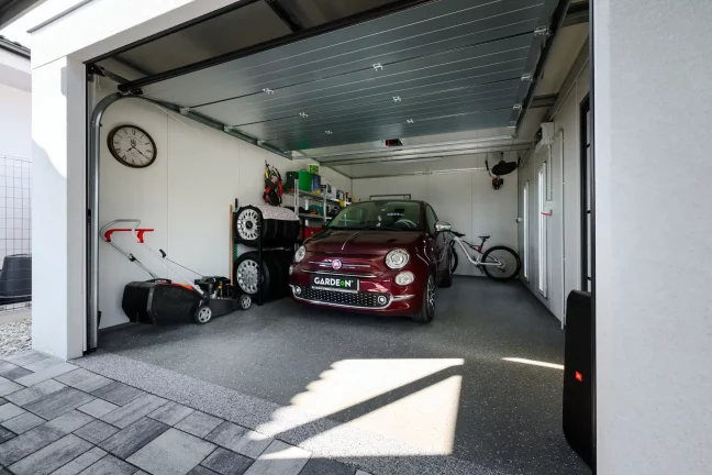 Innenansicht einer weißen Garage mit geöffnetem Rolltor, rotes Auto und Fahrrad im Inneren
