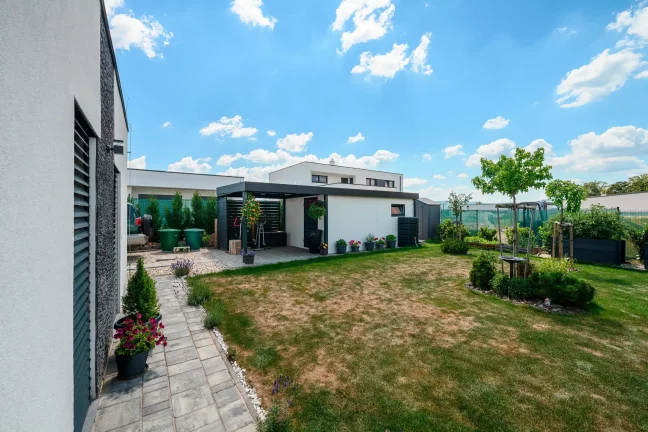 Gartenhaus mit weißem Putz und anthrazitfarbenem Carport im gepflegten Garten.