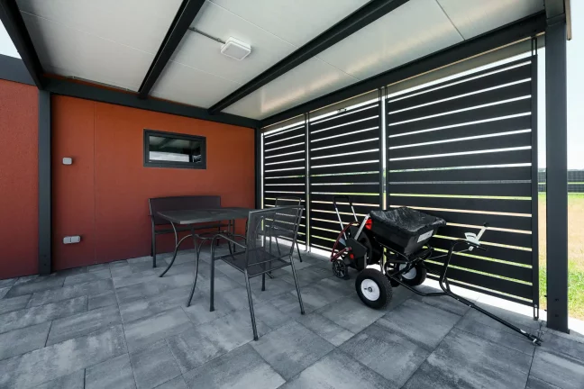Überdachte Sitzecke unter Carport mit anthrazitfarbener Metallfüllung und KABE Ziegelputz am Gartenhaus.