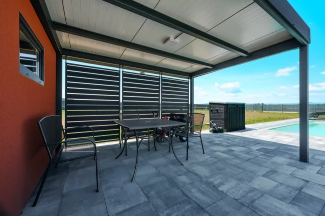 Carport mit anthrazitfarbener Metallwandfüllung am Pool mit Sitzbereich.