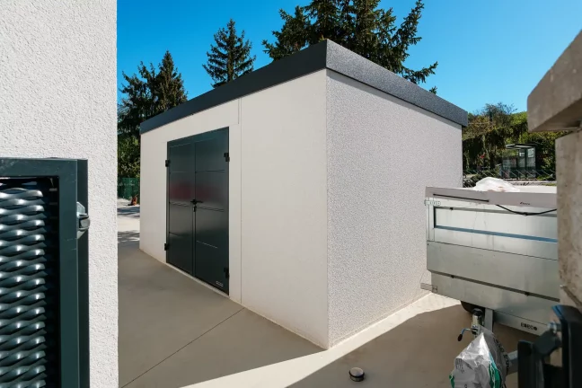 Minimalistisches Gartenhaus mit überdachtem Bereich neben Einfamilienhaus