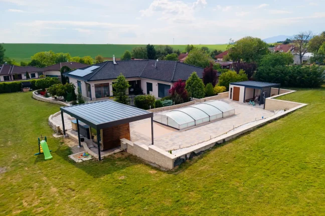 Luftaufnahme eines Gartenhauses mit Pool und Überdachung neben einem Einfamilienhaus, grüne Umgebung