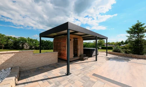 Freistehende anthrazitfarbene Pergola mit Flachdach auf einer gepflasterten Terrasse, grüner Garten im Hintergrund