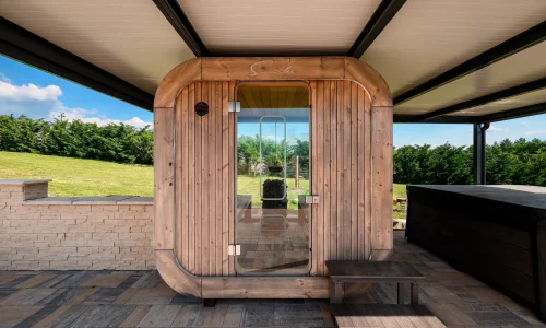 Blick aus dem Inneren einer anthrazitfarbenen Pergola auf eine Fasssauna mit Holztür und Whirlpool