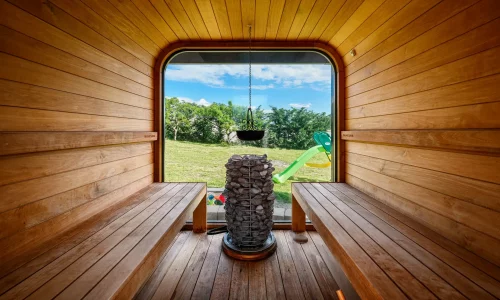 Innenansicht einer Fasssauna mit Holzverkleidung und Blick auf den grünen Garten
