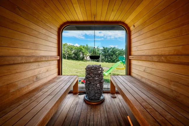 Innenansicht einer Fasssauna mit Holzverkleidung und Blick auf den grünen Garten