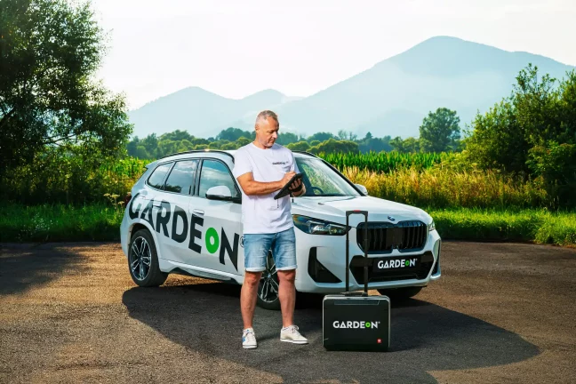 GARDEON-Agent mit Tablet, Firmen-BMW und Koffer in der Natur.