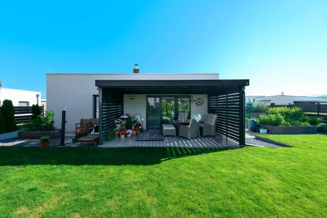 Anthrazitfarbene Pergola mit Metallfüllung am Einfamilienhaus mit Rasengarten.
