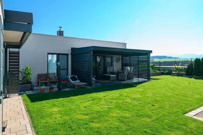 Anthrazitfarbene Pergola mit Metallfüllung am Einfamilienhaus mit Garten.