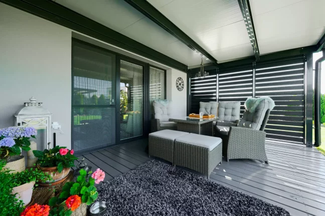 Anthrazitfarbene Pergola mit Metallamellen und Rattanmöbeln auf der Terrasse.