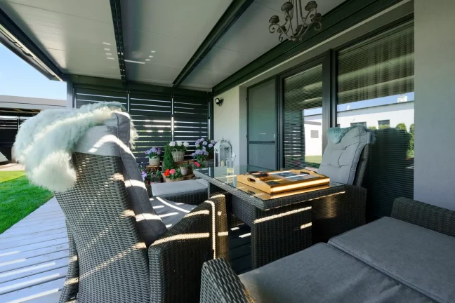 Innenansicht der anthrazitfarbenen Pergola mit Metallfüllung und Gartenmöbeln.