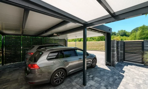 Blick vom Carport aus durch das geöffnete Tor auf eine Wiese