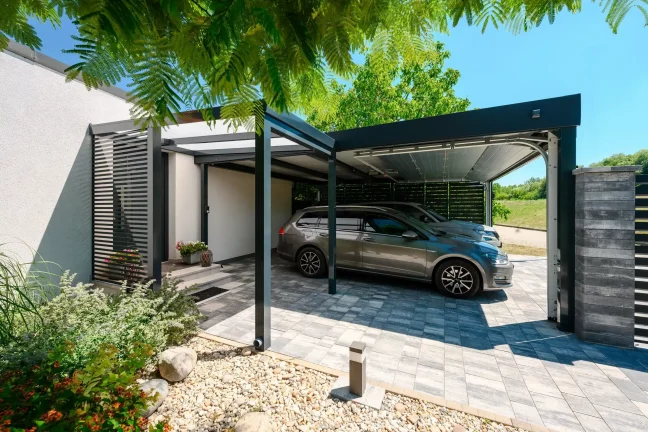 Auto unter dem Carport neben einer Steinsäule und einem Baumast