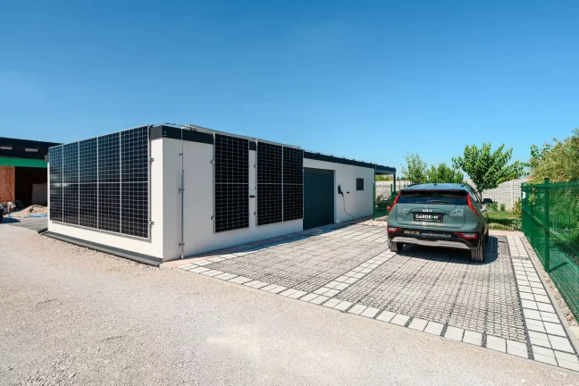 Blick auf das Haus mit Solarmodulen an der Wand, grünem Auto und Tor