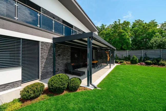 Haus mit Steinverkleidung und schwarzer Pergola über der Terrasse