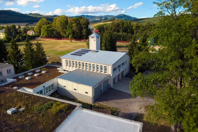 Drohnenaufnahme des Feuerwehrhauses mit neuer Garage und Turm vor den Bergen
