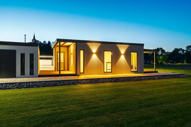 Beleuchtete Seitenwand des Tiny Houses mit Fenstern in der Dämmerung