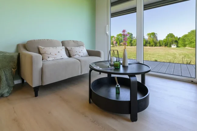 Sofa und runder Couchtisch am großen Fenster mit Blick in den Garten